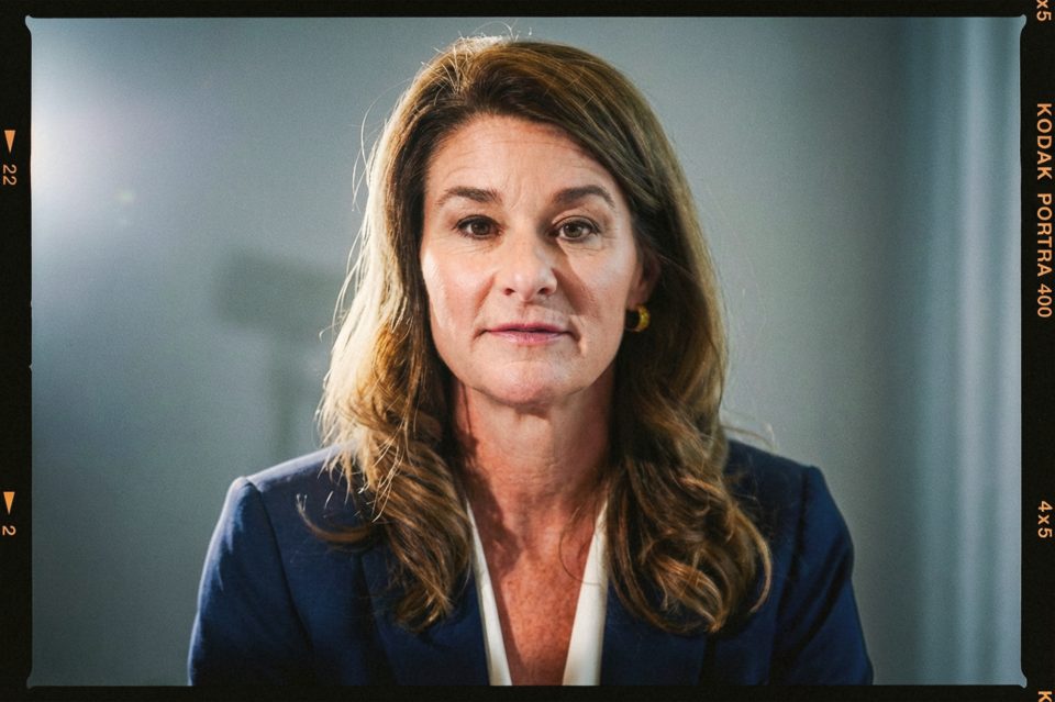 A woman with wavy brown hair, in a navy blazer and white blouse, looks directly at the camera against a neutral background. Captured by a DC portrait photographer, the film border adds a classic touch to the image.